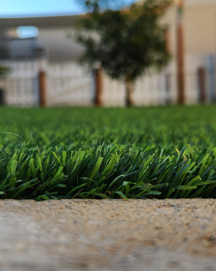 Low-angle view along an artificial grass edge against a concrete kerb, school buildings behind