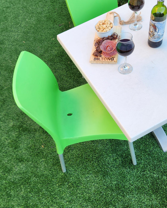 An outdoor table and green chair set up on artificial grass with a platter and glasses